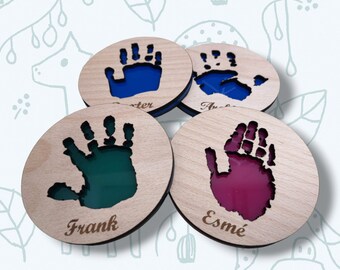 May include: Four wooden coasters with handprint cutouts filled with colored resin. Each coaster has a name engraved below the handprint: Carter, Frank, Esme, and Audrey.
