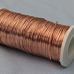 May include: A spool of rose gold wire, wound around a white plastic bobbin.