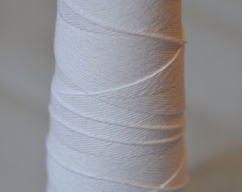 May include: A spool of white cotton thread wound around a black plastic bobbin.