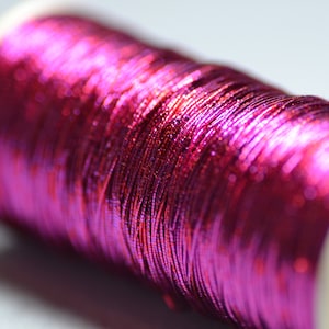 May include: A spool of metallic pink thread. The thread is wound tightly around the spool and has a shiny, iridescent finish.