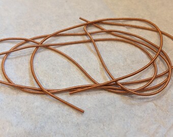 May include: A close-up of a bundle of copper-colored elastic cord. The cord is coiled and twisted together, creating a textured look.