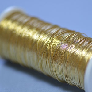 Può includere: Un'bobina di filo metallico dorato avvolto attorno a una bobina di plastica bianca.