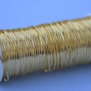 May include: A spool of gold metallic thread, wound tightly on a white plastic bobbin.