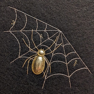 May include: A silver spider with a gold outline sits in the center of a gold web on a black background.