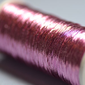 May include: A spool of metallic pink thread wound around a white plastic bobbin.