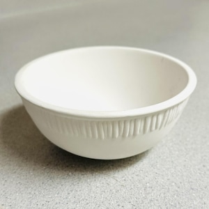 May include: A small, round, matte white ceramic bowl featuring a smooth interior and a textured exterior band near the base, characterized by a series of vertical, raised, parallel ridges that encircle the lower portion of the vessel.