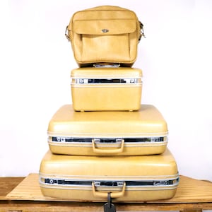 Könnte beinhalten: Ein Set aus vier Vintage-Gepäckstücken in hellgelber Farbe. Das Set beinhaltet einen kleinen, rechteckigen Handgepäckkoffer, einen größeren Koffer und eine passende Reisetasche.