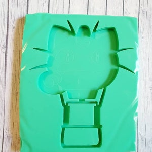 May include: Green silicone mold for making resin crafts. The mold is shaped like a hot air balloon with a cat's face on the top.