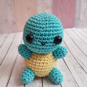 May include: A crocheted turtle toy with a light blue shell and a yellow belly. The toy has black eyes and a small smile.