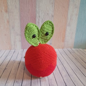 May include: A red crocheted apple with green crocheted leaves and black button eyes.