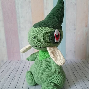 May include: Green crocheted plush toy with a pointed hat and white ears. The toy has a red eye with a white outline.