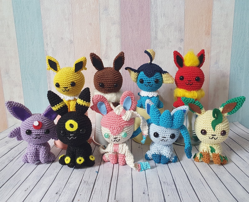 May include: A collection of eight crocheted Pokemon characters, including Pikachu, Eevee, and Charmander. The characters are all different colors and have different expressions on their faces.