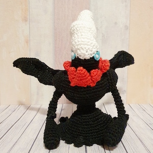 Könnte beinhalten: Schwarzes gehäkeltes Amigurumi-Spielzeug mit roten und weißen Details. Das Spielzeug hat einen weißen gehäkelten Hut und blaue Augen.