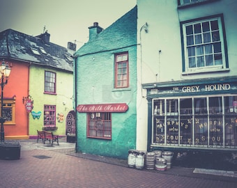 May include: A vintage-style photo of a street scene with colorful buildings. The buildings have storefronts with signs that read "The Fish Market" and "The Grey Hound".