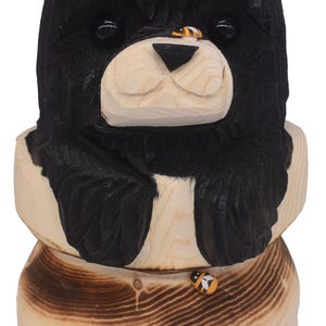 May include: Wooden bear sculpture with a black head and paws, perched atop a honey pot. The word "HONEY" is painted on the pot. A small bee is painted on the bear's nose and the pot.
