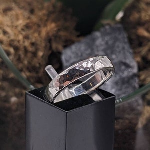 May include: A silver hammered band ring on a black display stand. The ring is made of metal and has a textured surface.