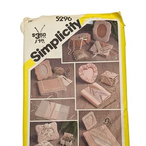 May include: A vintage Simplicity sewing pattern envelope, featuring a yellow and white design. The envelope showcases various craft projects, including decorative boxes and frames. The text "Simplicity" is prominently displayed.