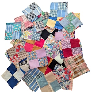 May include: A collection of assorted fabric squares, each composed of four smaller patches sewn together. The squares feature a variety of patterns including floral prints, gingham, stripes, plaids, and solid colors in shades of blue, red, pink, yellow, and black.