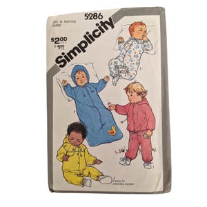May include: Simplicity sewing pattern for 18-month-old babies. The pattern features illustrations of babies in various outfits, including a blue sleep sack with a duck, a pink jumpsuit, and a yellow hooded outfit.