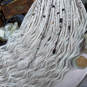 May include: White synthetic dreadlocks with wavy texture, adorned with brown leather cord, beads, and metal charms.