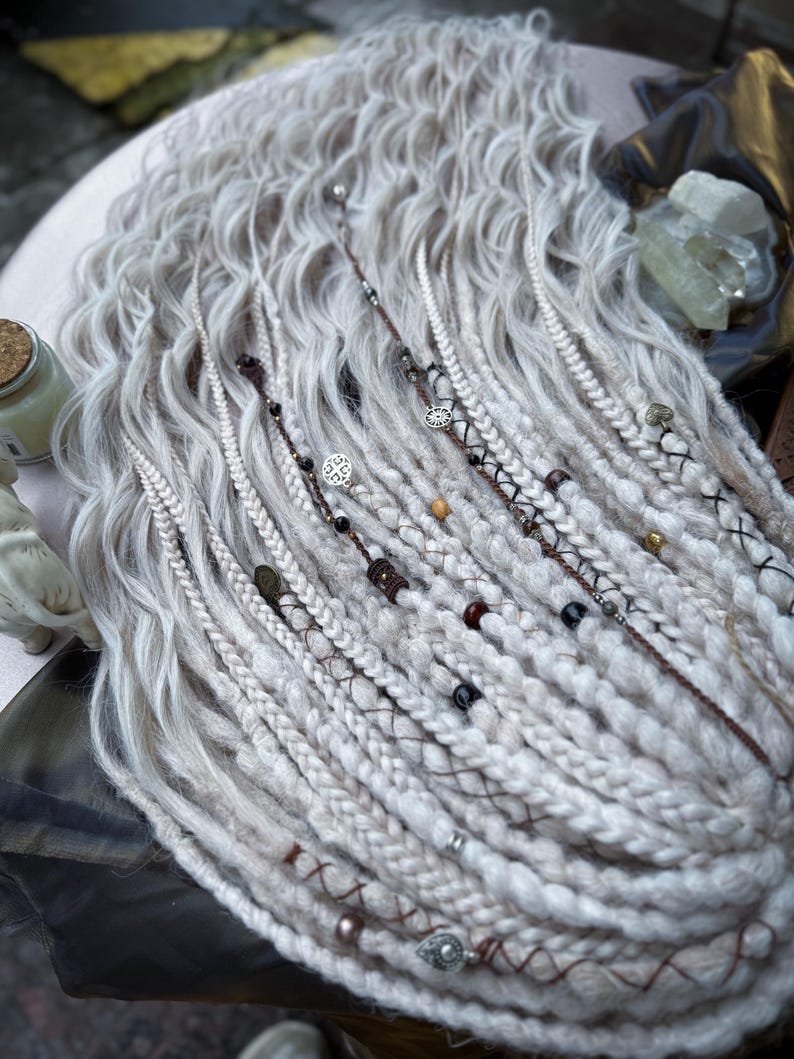 May include: White synthetic dreadlocks with brown, black, and silver beads and charms. The dreadlocks are long and wavy.