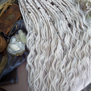 May include: White synthetic dreadlocks with brown and silver beads. The dreadlocks are wavy and have a natural look.