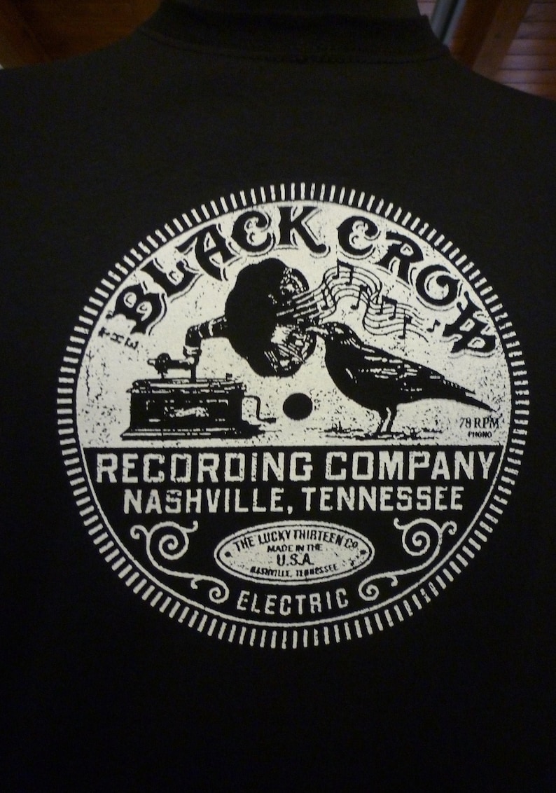 May include: Black and white graphic of a vintage record player with a crow perched on top. The graphic is surrounded by a circle with the text "Black Crow Recording Company Nashville, Tennessee" and "The Lucky Thirteen Co. Made in the U.S.A. Electric".