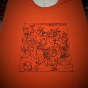 May include: A black and white illustration of a group of anthropomorphic animals drinking and socializing in a tavern setting. The animals are dressed in medieval clothing and are holding mugs of beer. The illustration is printed on a red t-shirt.