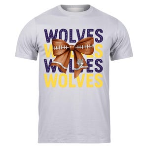 May include: A light gray t-shirt featuring the word "WOLVES" in purple and yellow. A brown bow with football stitching and a wolf head graphic is centered on the shirt.