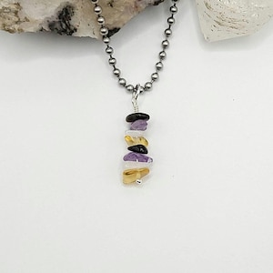 May include: A silver chain necklace with a pendant made of stacked, small, irregularly shaped gemstones. The gemstones are purple, white, black, and yellow.