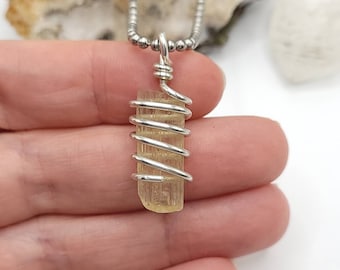 Op de afbeelding: Een zilveren, met draad omwikkelde hangerketting met een lichtgeelbruin, rechthoekig kristal. Het kristal is ongeveer 2,5 cm lang en hangt aan een zilveren kralenketting. De hanger is een natuurlijke edelsteen, geschikt voor dagelijks gebruik.