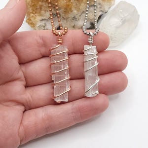 May include: Two selenite crystal necklaces. One features a copper-colored wire wrap and chain, the other a silver-colored wire wrap and chain. Both have a rectangular crystal pendant. The necklaces are displayed against a white background.