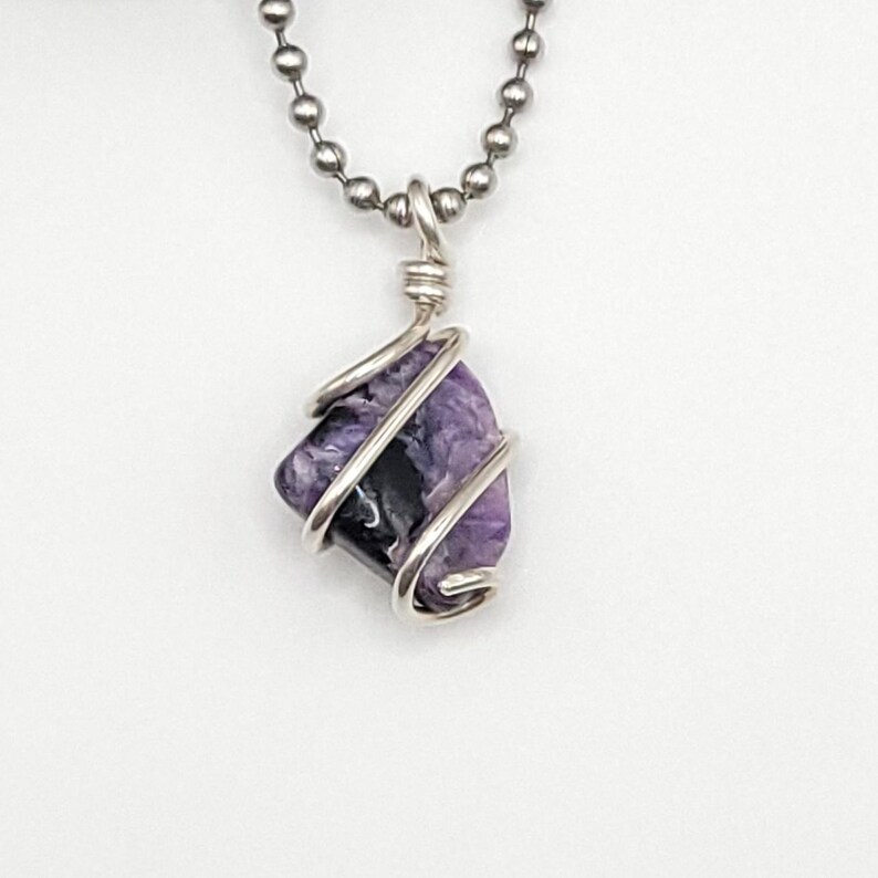 May include: A silver chain necklace with a purple and black charoite gemstone pendant wrapped in silver wire.