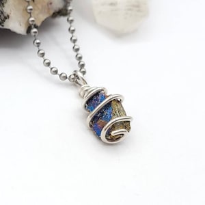May include: A silver-toned necklace featuring a pendant with a colorful, iridescent stone wrapped in wire. The stone displays hues of blue, gold, and purple. The chain is a ball chain style, and the pendant is centered.