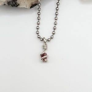 May include: A silver chain necklace with a small, dark red gemstone wrapped in silver wire.