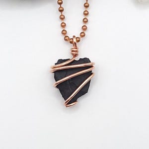 May include: A black shungite pendant wrapped in copper wire, hanging from a copper chain.