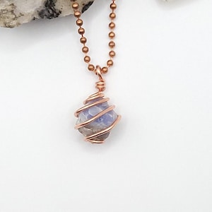 May include: A copper-colored wire-wrapped pendant necklace featuring a light blue and gray stone. The stone is encased in a spiral of copper wire and hangs from a copper ball chain. The background is white.