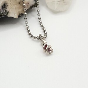May include: A silver chain necklace with a small, red gemstone pendant wrapped in silver wire.
