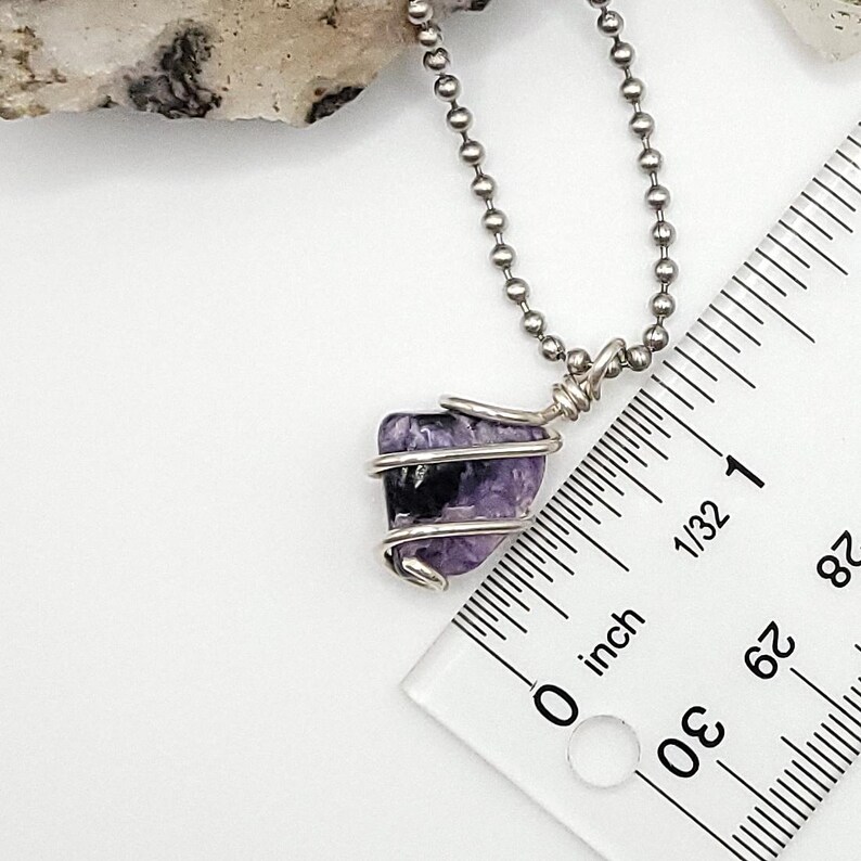 May include: A silver chain necklace with a purple and black charoite crystal pendant wrapped in silver wire. The pendant is about 1/2 inch in size.