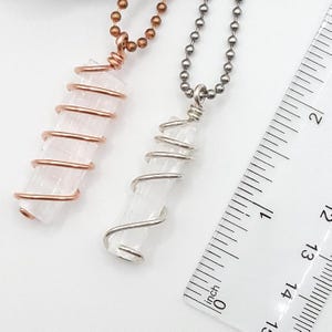 May include: Two crystal pendant necklaces. One features a clear crystal wrapped in copper wire, the other in silver wire. The crystals are approximately 1.5 inches long. A ruler is in the background, showing inch measurements.