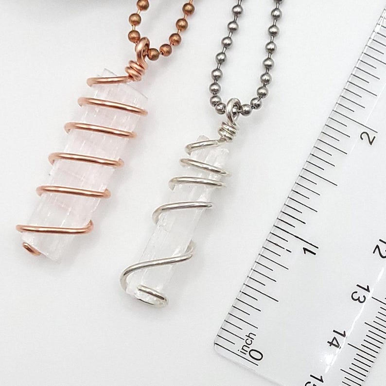 May include: Two crystal pendant necklaces. One features a clear crystal wrapped in copper wire, the other in silver wire. The crystals are approximately 1.5 inches long. A ruler is in the background, showing inch measurements.