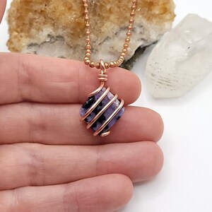 charoite wrapped with copper wire on a white background in hand