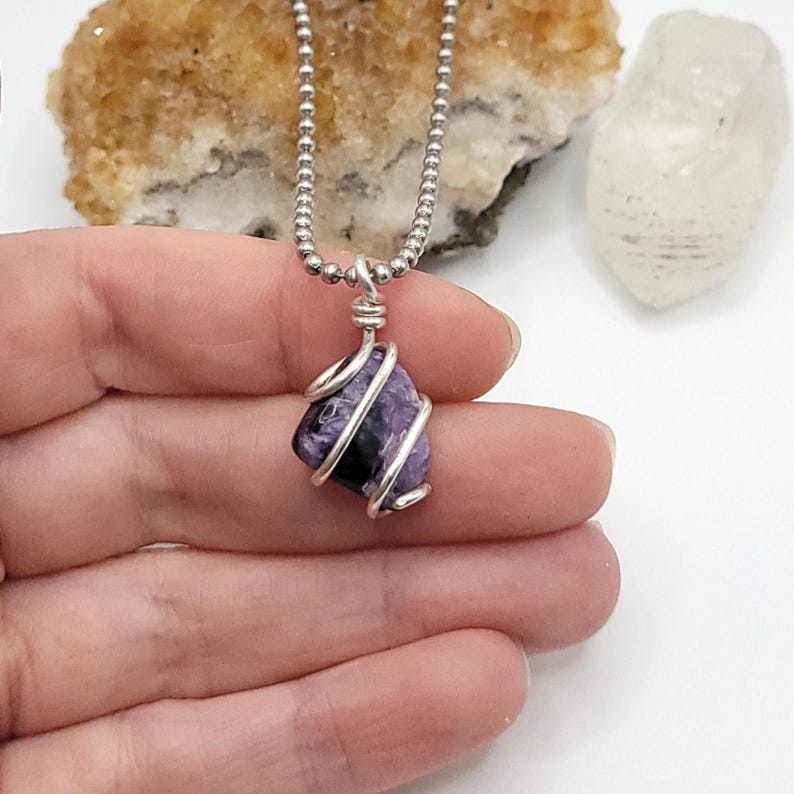 May include: A silver chain necklace with a charoite and silver wire-wrapped pendant. The pendant features a natural purple stone.