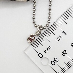 May include: A silver chain necklace with a small pink gemstone wrapped in silver wire. The necklace is measured against a ruler, showing the gemstone is less than 1/2 inch in size.