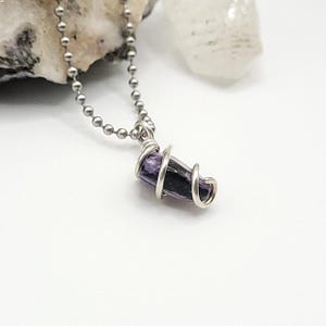 May include: A silver chain necklace with a purple and black charoite stone pendant wrapped in silver wire.