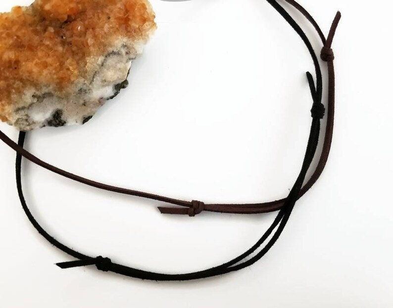 May include: A close-up of a brown and black leather cord necklace. The cord is tied in a knot at the top and the ends are frayed.