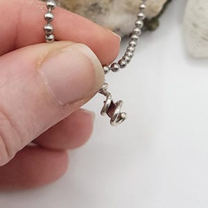 May include: A silver chain necklace with a small, spiral-shaped pendant featuring a purple gemstone.