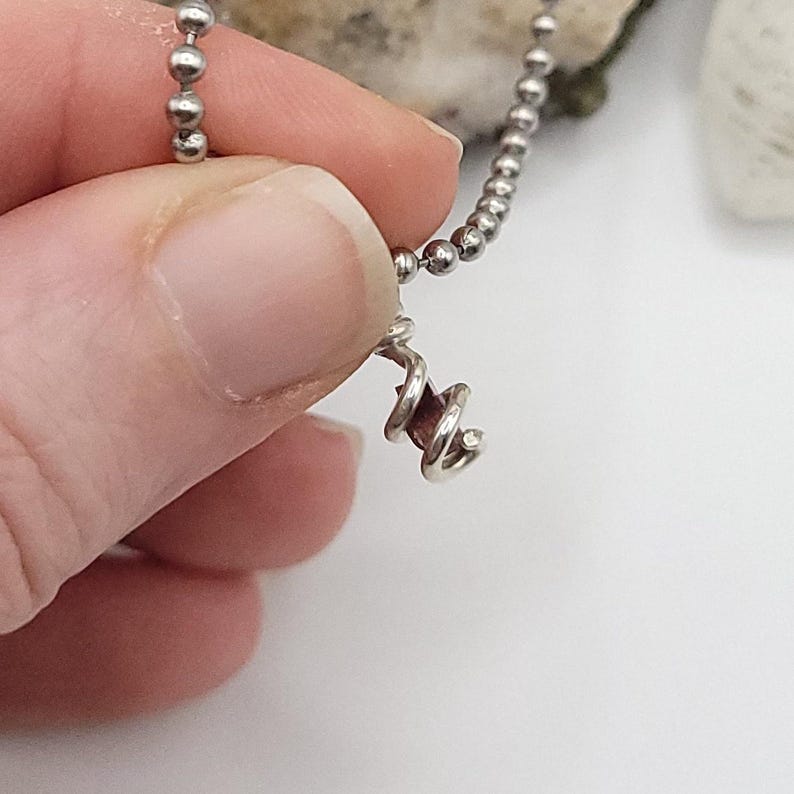 May include: A silver chain necklace with a small, spiral-shaped pendant featuring a purple gemstone.