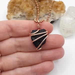 May include: A black shungite stone wrapped in copper wire, hanging from a copper chain necklace.
