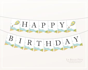 May include: A white banner with the words "HAPPY BIRTHDAY" in black letters. The banner is decorated with a blue and green sky with white clouds and yellow and pink hills. There are two illustrations of a character in a hot air balloon on either end of the banner.
